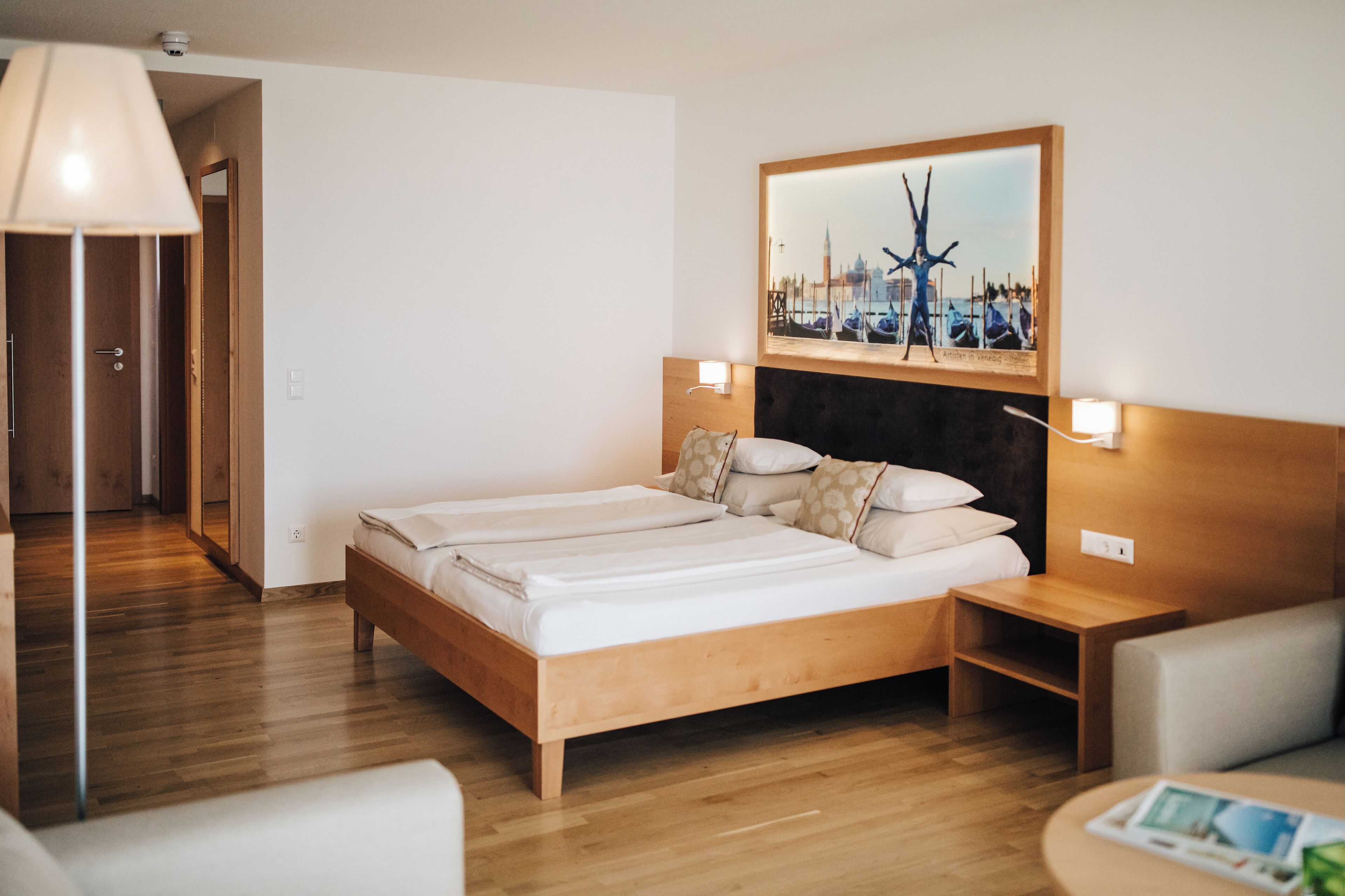 Habitación de hotel con una cama de madera, dos mesitas de noche, una lámpara y un cuadro en la pared.