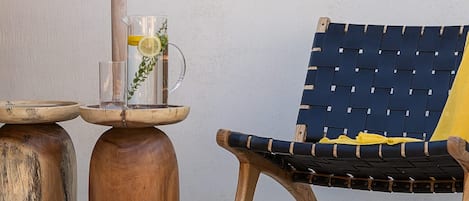 A wooden bench with a woven backrest, a clear glass pitcher with a yellow cloth, and two wooden stools with a metal base.