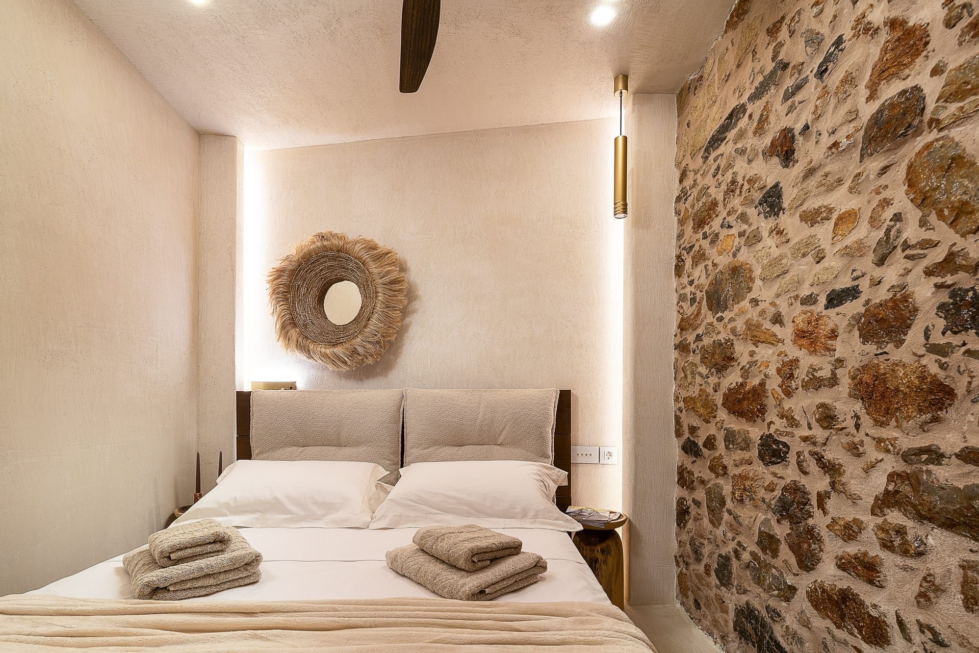Una habitación de hotel con una cama, un espejo redondo montado en la pared y una pared de piedra.