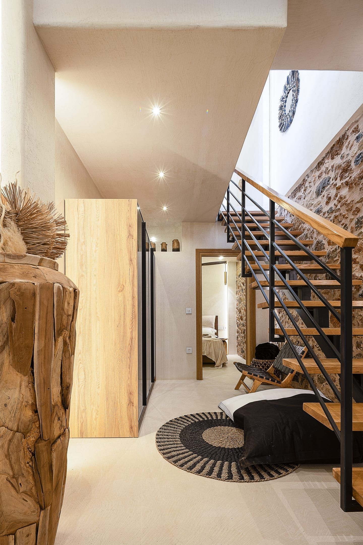 A modern interior with a wooden staircase, a round rug, and a stone wall.