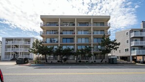 A multi-story residential building with balconies, a parking lot, and a clear sky. - New For 2025! Charming 1 bedroom condo oceanblock in North OC (Ocean City)