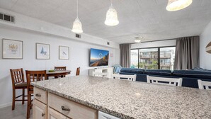 A modern kitchen with granite countertops, wooden chairs, a dining table, and a large island. - New For 2025! Charming 1 bedroom condo oceanblock in North OC (Ocean City)