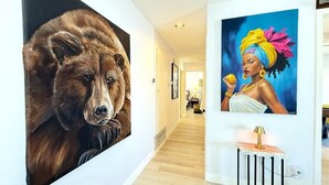 En hall med två stora tavlor på väggarna, ett litet bord med en lampa och ett trägolv.