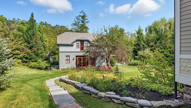 A two-story house with a stone pathway leading to the front door, surrounded by a well-maintained garden and trees. - Cliffwood Cottage by Evergreen Home (Lenox)