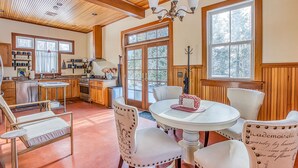 A spacious kitchen with wooden cabinets, a dining area with a round table and white chairs, and large windows allowing natural light. - Cliffwood Cottage by Evergreen Home (Lenox)