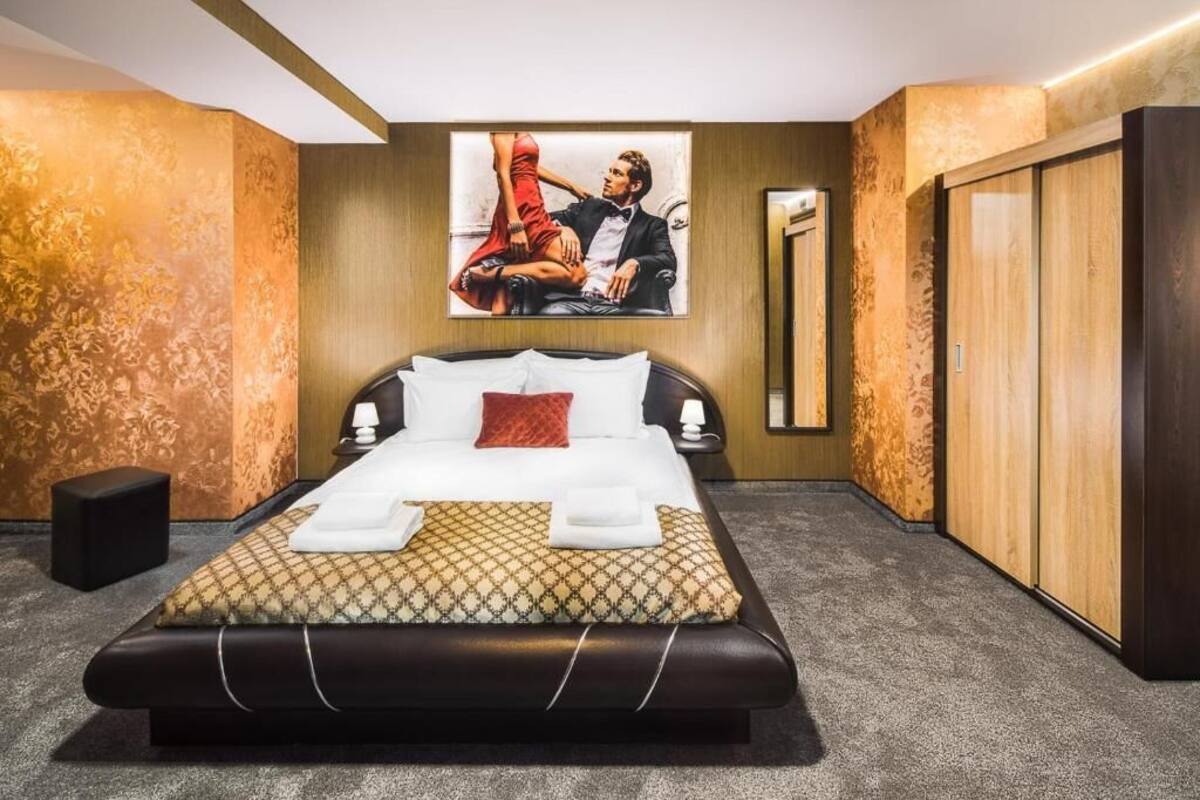 A hotel room with a large bed, a wall-mounted TV, a wardrobe, and a small bedside table.
