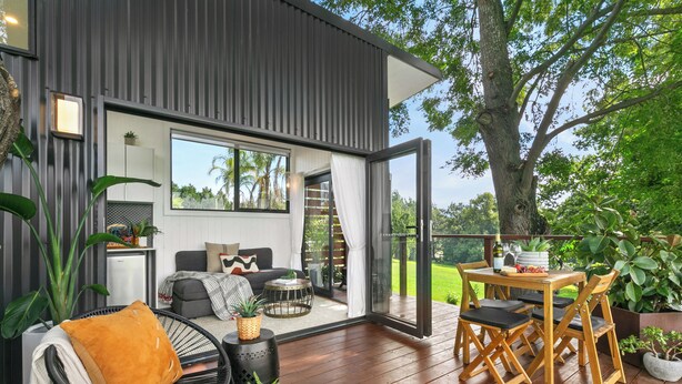 Un espacio exterior moderno con terraza de madera, un sofá, una mesa de comedor con sillas y plantas en macetas.