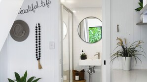 Un baño con un lavamanos blanco, un espejo, una planta y una pared decorada.