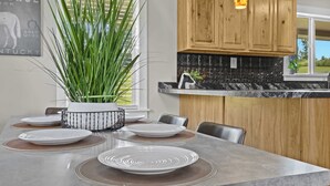 Une table à manger dressée avec des assiettes et des sets de table, entourée de chaises, dans une pièce dotée de meubles en bois et d’une fenêtre.