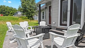 Une terrasse avec des fauteuils Adirondack et une table, une véranda grillagée et une vue sur une maison et la verdure.