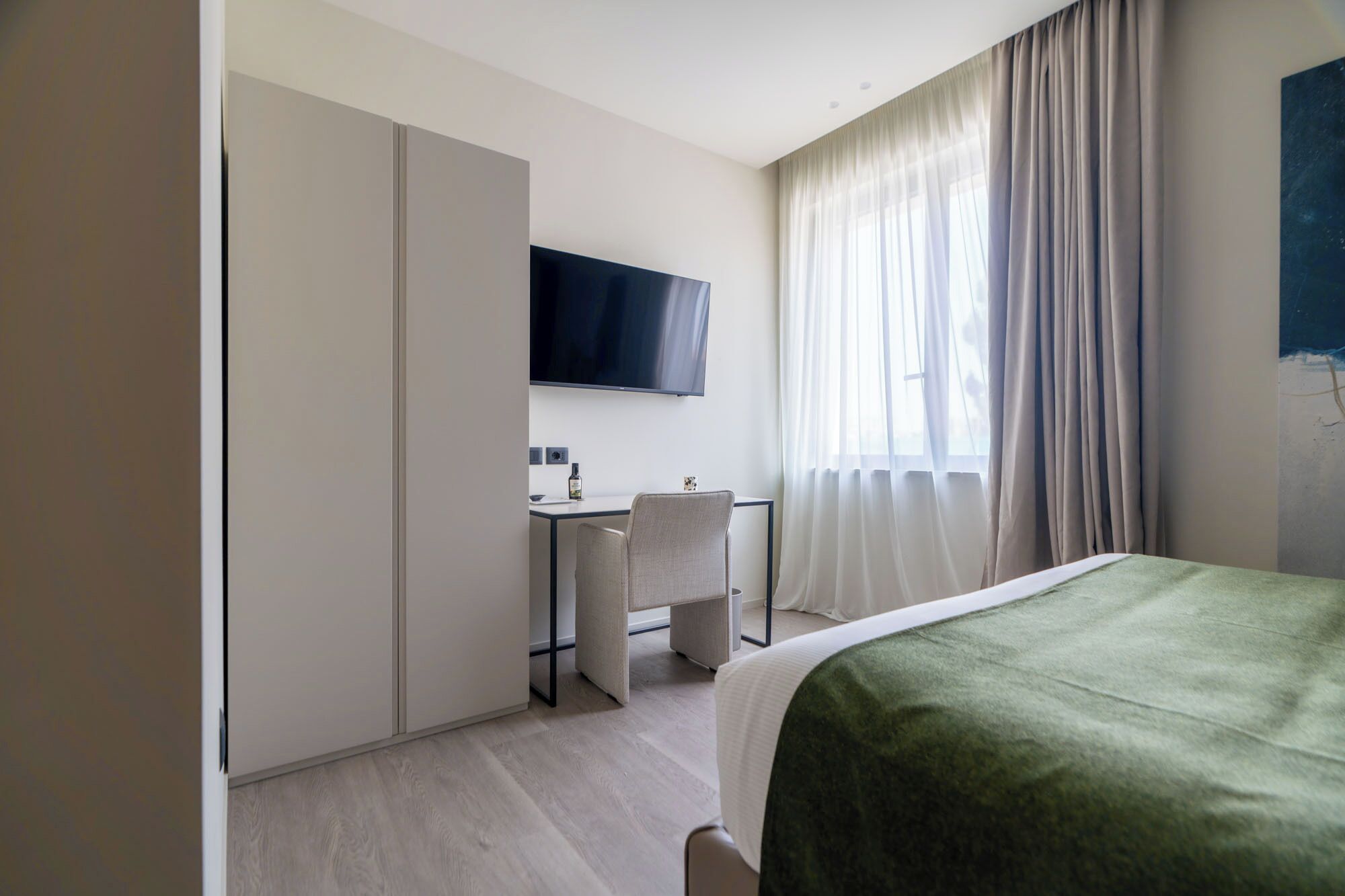 A hotel room with a bed, a desk, a chair, a TV, and a window with curtains.