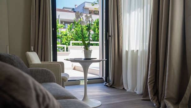 A modern living room with a sofa, a small table with a plant, and a view of a balcony with greenery. - Villa Verdeoro (Montesilvano)