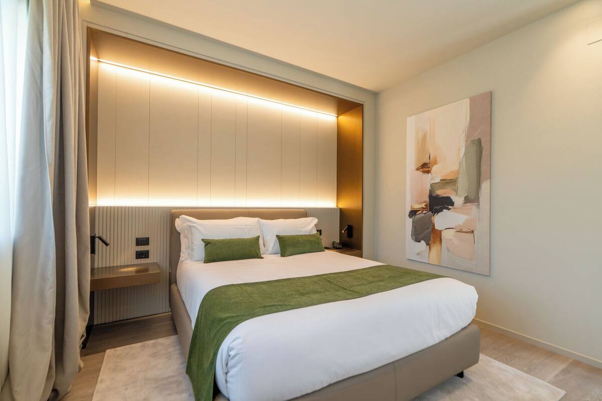 A modern bedroom with a large bed, a bedside table, a nightstand, and a wall-mounted light fixture.