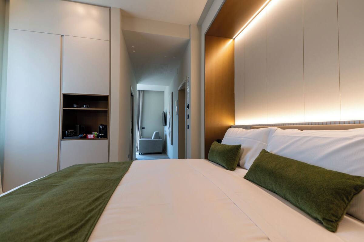 A modern hotel room with a large bed, a built-in wardrobe, and a seating area in the background.