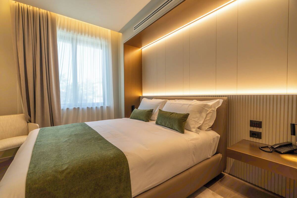 A hotel room with a large bed, a bedside table with a phone, and a window with curtains.