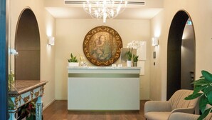 A reception area with a chandelier, a reception desk, and a large decorative painting. - Villa Verdeoro (Montesilvano)