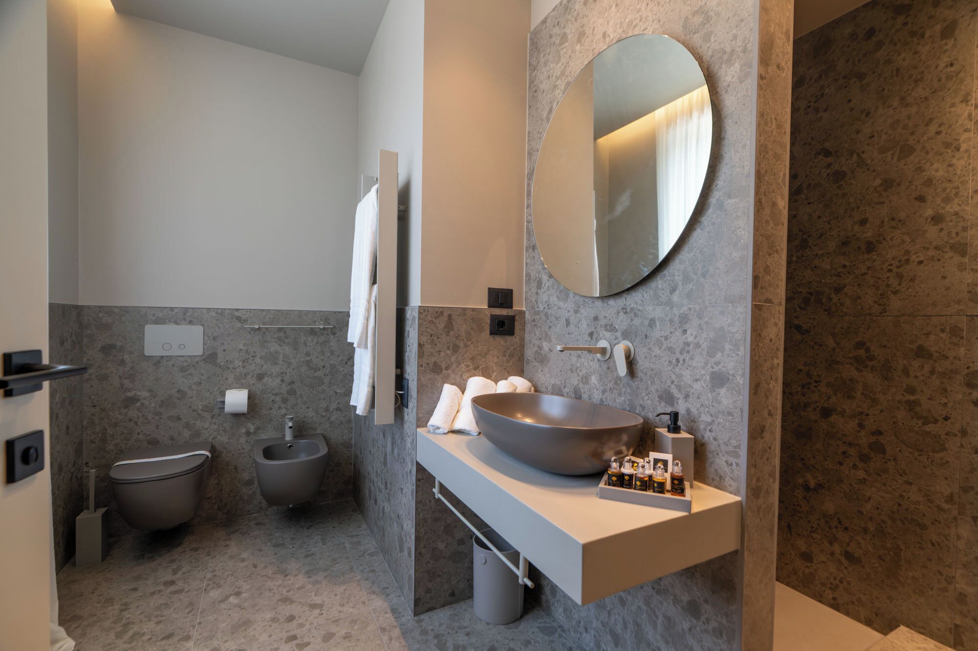 A modern bathroom with a large round mirror, a vessel sink, and a bidet.