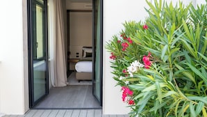 A hotel room with a bed, a small table, and a window. There is a balcony with a plant and flowers. - Villa Verdeoro (Montesilvano)