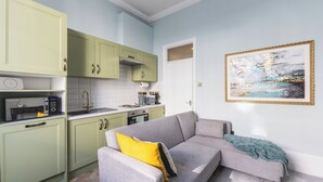 A modern kitchen with green cabinets, a gray sofa with a yellow pillow, and a painting on the wall. - Chic flat in Central London near Victoria Station - SW1 (London)