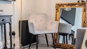 A room with a white armchair, a large ornate mirror, and a radiator. - Chic flat in Central London near Victoria Station - SW1 (London)