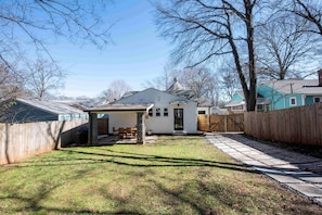 A backyard with a covered patio, a wooden fence, and a house with a gabled roof.