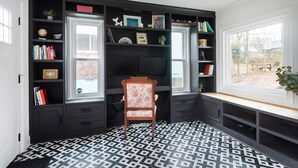 Ein Zimmer mit einem schwarz-weiß gemusterten Boden, einem Holzstuhl und einem Bücherregal voller Bücher und Dekorationsgegenstände.