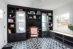 A room with a black and white patterned floor, a wooden chair, and a bookshelf filled with books and decorative items.