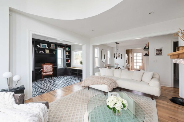 A spacious living room with a white sofa, a glass coffee table with flowers, a patterned rug, and a black and white patterned floor.
