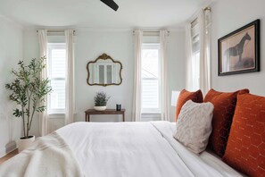 A bedroom with a large bed, a mirror, a potted plant, and a window with curtains.