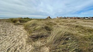 Ein Sandstrand mit Dünen und ein weiter Blick auf eine Stadt mit Häusern.