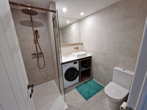 Un baño moderno con ducha acristalada, lavadora, lavamanos e inodoro.