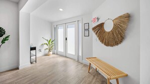 Un pasillo moderno con suelo de madera, un banco, plantas en macetas y un adorno en la pared.