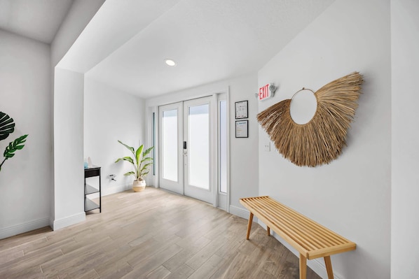 Un couloir moderne avec un plancher en bois, un banc, des plantes en pot et un objet décoratif fixé au mur.