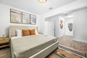 Un dormitorio con una cama grande, una mesita de noche y un espejo montado en la pared. Hay tres obras de arte enmarcadas en la pared sobre la cama.