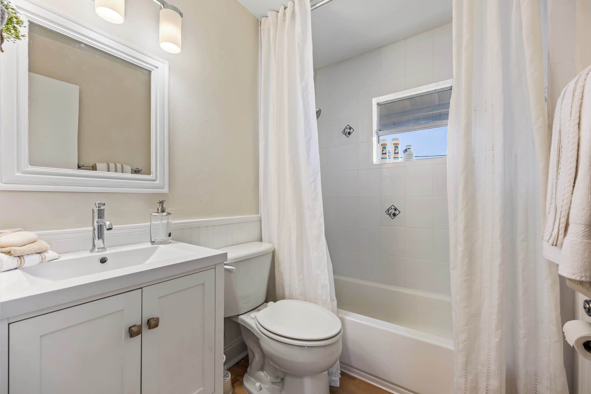 A bathroom with a white sink, mirror, toilet, and bathtub.
