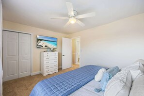 Quarto com cama, ventilador de teto, cômoda, armário e pintura de uma praia.