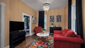 A living room with a flat-screen TV, red sofas, a coffee table, and a chandelier. - Pet-friendly 1917 Art Deco 2BR in Olympia, walkable downtown with workspace, parking, and modern comfort (Olympia)