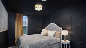 A bedroom with a large bed, a nightstand, a chandelier, and a window with curtains. - Pet-friendly 1917 Art Deco 2BR in Olympia, walkable downtown with workspace, parking, and modern comfort (Olympia)