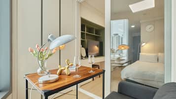 A modern hotel room with a wooden desk, a lamp, a vase with flowers, and a bed with a view of the city.