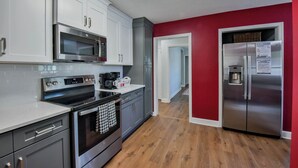 A modern kitchen with white cabinets, stainless steel appliances, and a red accent wall. - Tide on 19th- 4BR/2BA, Large Patio, Fire Pit & Smart TVs! (Northport)