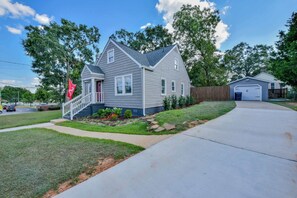 A two-story house with a front porch, a garage, and a well-maintained lawn. - Tide on 19th- 4BR/2BA, Large Patio, Fire Pit & Smart TVs! (Northport)