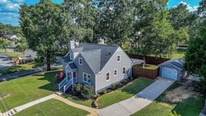 A two-story house with a front porch, a garage, and a well-maintained lawn. - Tide on 19th- 4BR/2BA, Large Patio, Fire Pit & Smart TVs! (Northport)