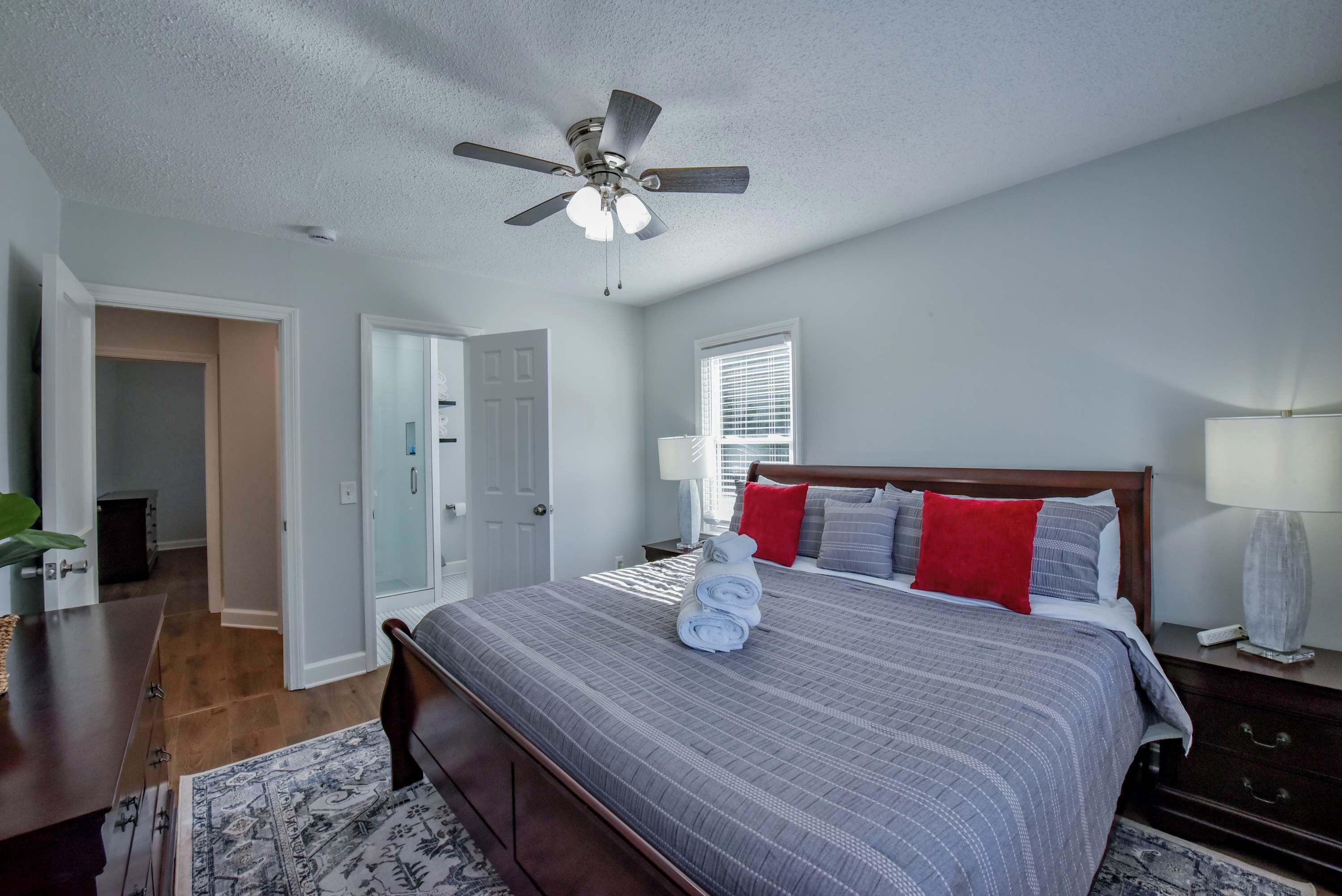 A bedroom with a bed, a ceiling fan, a nightstand, a lamp, and a window with blinds.