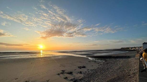 Een strand bij zonsondergang met een heldere lucht en een gebouw in de verte.
