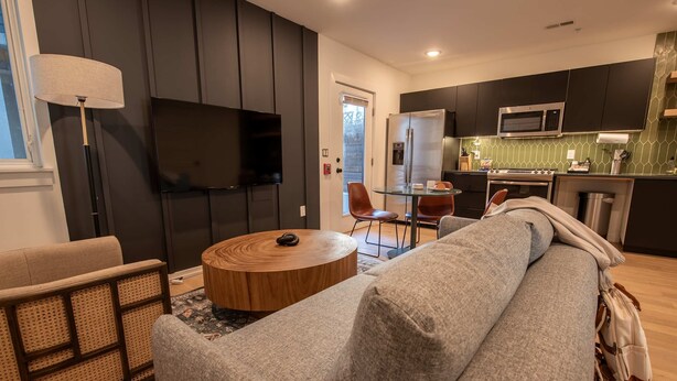 A modern living room with a grey sofa, a round wooden coffee table, and a TV mounted on the wall.