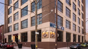 Een meerlaags gebouw met een hoingang, grote ramen en een bordesbord dat nieuwe appartementen adverteert.