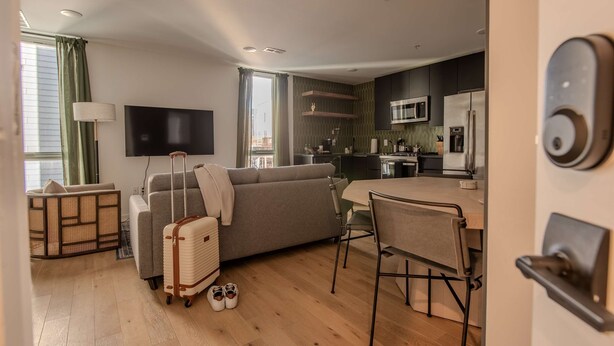 A modern living room with a sofa, a TV, a dining table with chairs, and a kitchen area with a microwave and refrigerator. - Sosuite NEW 2BR Apt w W D Split Level (Philadelphia)