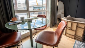 Una habitación moderna con una mesa de vidrio, sillas de cuero, un sofá y vistas a una obra en construcción a través de un gran ventanal.