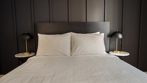Una cama bien hecha con sábanas blancas, dos mesitas de noche con lámparas y un cabecero de paneles oscuros.