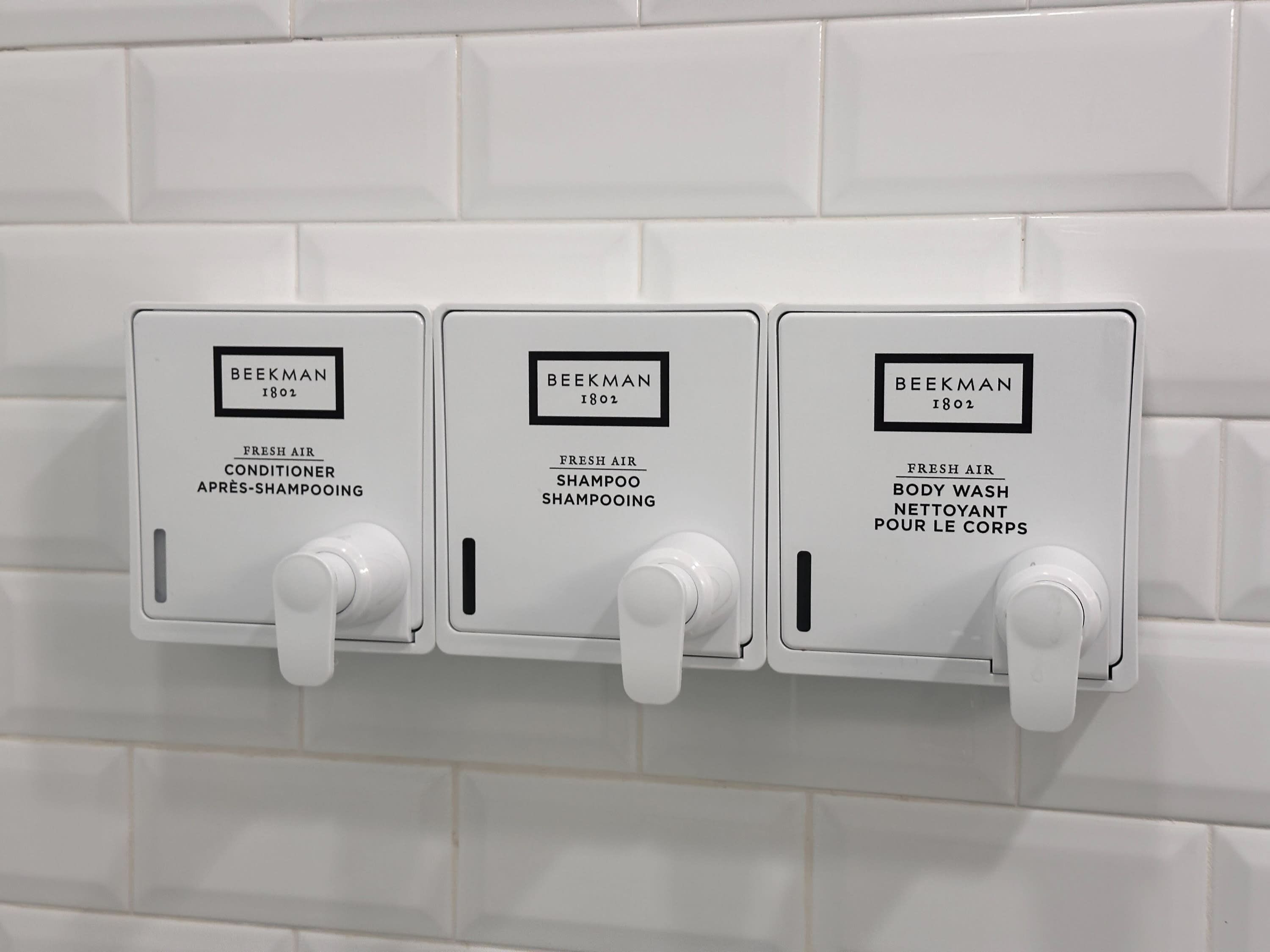 Three wall-mounted dispensers labeled 'BEEKMAN 1802' for fresh air conditioner, shampoo, and body wash.